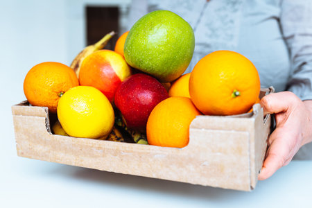 Fruits in a box in the hands of a young woman.の写真素材