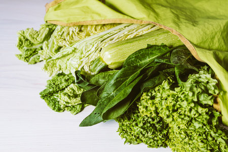 Green vegetables in a reusable shopping bag on a white wooden background.の写真素材