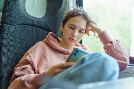 Young woman using mobile phone while traveling by train. Teenage girl using smartphone in train.の写真素材