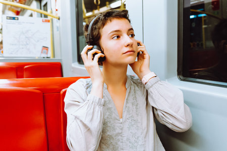 Travel by train listening to music. teenage girl with short cropped hair, smile on face, wearing wireless headphones, is riding train or subway car, enjoying music. travel conceptの写真素材