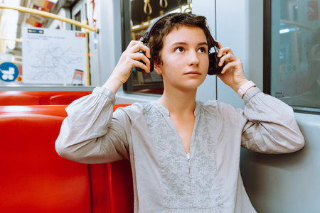 Travel by train listening to music. teenage girl with short cropped hair, smile on face, wearing wireless headphones, is riding train or subway car, enjoying music. travel conceptの写真素材