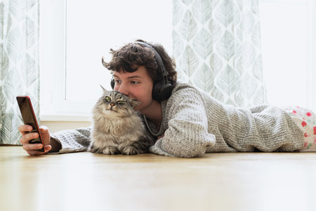 Young woman with cat in headphones lying on the floor at home.の写真素材