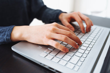 Close-up image of female hands typing on laptop keyboard at desk
