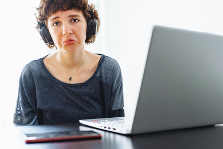 sad teenager girl, in headphones, with an offended expression, sits in front of laptop, upsetの写真素材