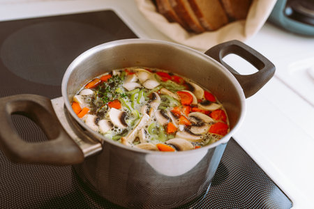 Chicken soup with mushrooms and vegetables in a pot on the kitchen table