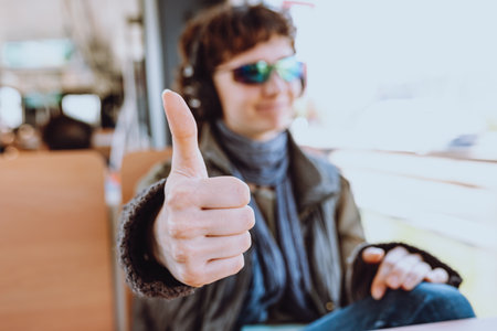 Thumb up shows lovely young girl in sunglasses, headphones, traveling in train or bus. blurred background, spot focusの写真素材