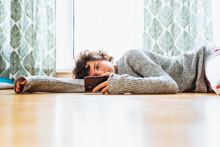 Young woman lying on the floor and using mobile phone at home.の写真素材