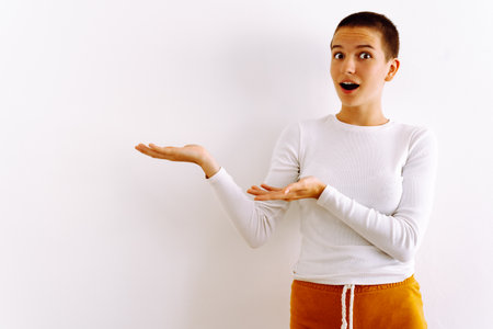 Excited attractive teen girl in white t-shirt pointing to copy space next to her, on white backgroundの写真素材