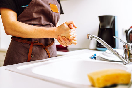 Unrecognizable female figure in brown work apron in kitchen near kitchen sinkの写真素材