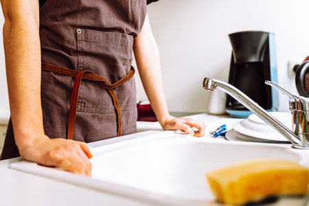 Unrecognizable female figure in brown work apron in kitchen near kitchen sinkの写真素材