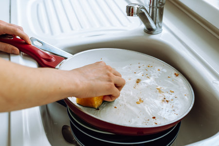 Women's hands wash greasy, burnt frying pan, with ceramic coating, washcloth and dishwashing detergent, in home kitchen. concept routine, manual housework, washing dishesの写真素材
