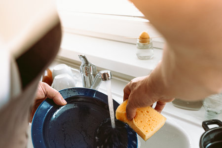 Middle-aged man, muscular build, wearing brown kitchen apron, washing dishes in kitchen kitchen, concept male householder, household choresの写真素材