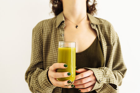 Hands girl with green manicure, hold glass fresh smoothie apple, spinach, celery, kiwi. girl's clothes are green tone, background light wall. Refreshing smoothie green vegetables, fruits, breakfastの写真素材