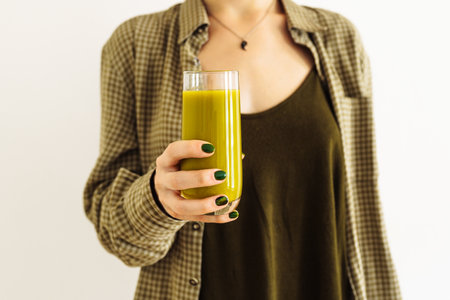 Hands girl with green manicure, hold glass fresh smoothie apple, spinach, celery, kiwi. girl's clothes are green tone, background light wall. Refreshing smoothie green vegetables, fruits, breakfastの写真素材