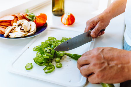 Man's hands cut peppers with knife on cutting board, slicing ingredients for pizza or saladの写真素材