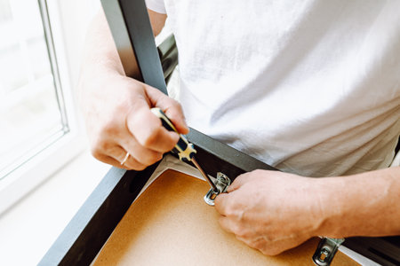 Close-up man's hand with screwdriver repairing wooden chair. concept home master, handyman for an hour, housework. man fixes chair with screwdriver, screwing screwの写真素材