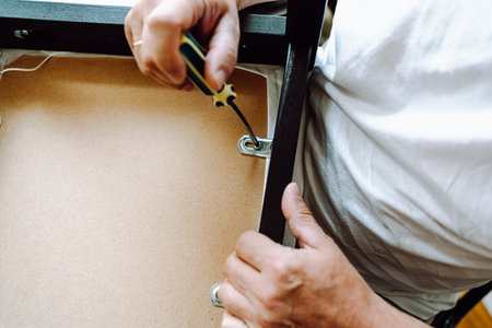 Close-up man's hand with screwdriver repairing wooden chair. concept home master, handyman for an...