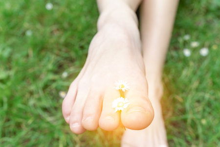 Womens slender bare feet on green grass with daisiesの写真素材