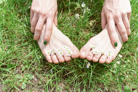 Womens slender bare feet on green grass with daisiesの写真素材