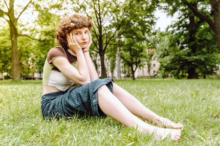 Portrait of attractive teen girl model smiling sitting on grass in city parkの写真素材