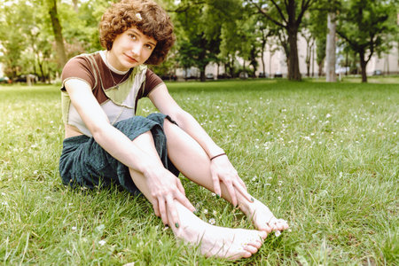 Portrait of attractive teen girl model smiling sitting on grass in city parkの写真素材