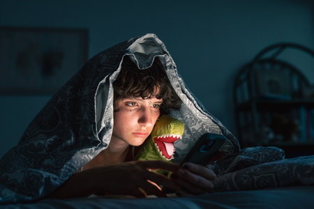 portrait teenage girl sitting under covers on bed, using phoneの写真素材