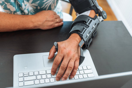 Man with adjustable articulated elbow orthosis typing on laptop keyboard