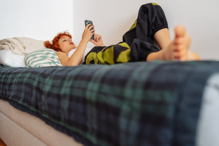 Teen girl lying on bed using phoneの写真素材