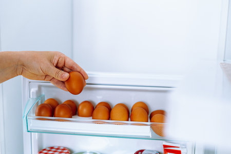Closeup human hands put chicken eggs in egg-laying compartment in refrigeratorの写真素材