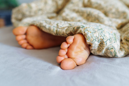 Bare feet young woman under blanketの写真素材