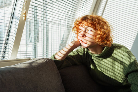 young red-haired woman in living room on sofa using phoneの写真素材