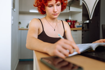 portrait red-haired teenage girl sitting at table in room using computerの写真素材