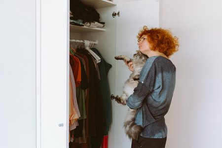 red-haired teenage girl and big cat choose things from closetの写真素材