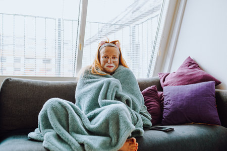 portrait middle-aged woman with cosmetic mask on face on sofa at homeの写真素材