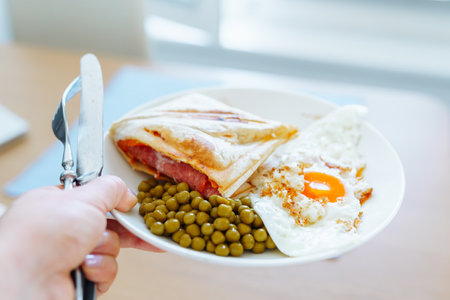 breakfast scrambled eggs hot sandwich with ham and cheese, green peas, legumes on plateの写真素材