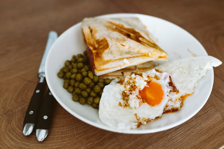 breakfast scrambled eggs hot sandwich with ham and cheese, green peas, legumes on plateの写真素材