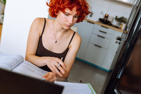 portrait red-haired teenage girl sitting at table in room using computer