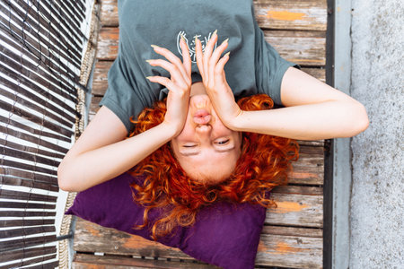 portrait red-haired curly young woman enjoying relaxation on balcony or terraceの写真素材