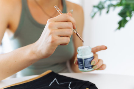 young woman draws picture on clothes with paints, handmade craft work. Customizationの写真素材