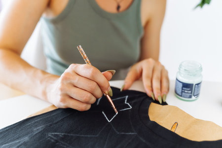 young woman draws picture on clothes with paints, handmade craft work. Customizationの写真素材