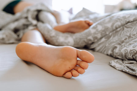 young woman lies on bed with bare feet uncovered by blanket. feet close upの写真素材