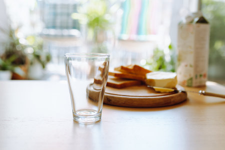 An empty glass stands on table, in background there is bread, butter, milk. Breakfastの写真素材