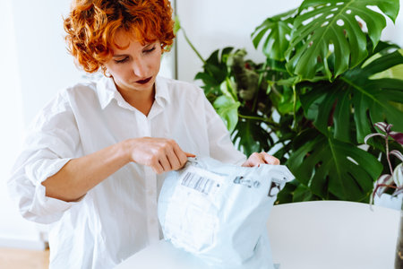 young red-haired attractive woman unpacking parcel at homeの写真素材