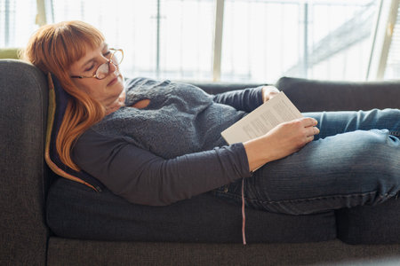 sleeping middle aged woman lying on sofa with bookの写真素材