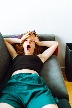 young red-haired woman tired lies on sofaの写真素材