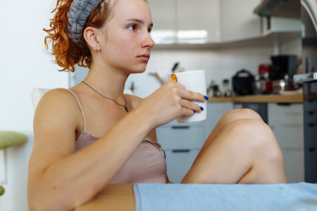 portrait young red-haired woman in morning, drinking coffee sitting on chair in dining roomの写真素材
