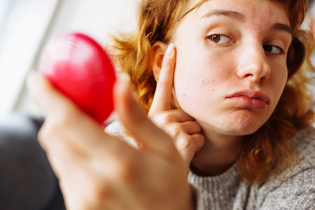 young woman looks at problematic facial skin in mirrorの写真素材