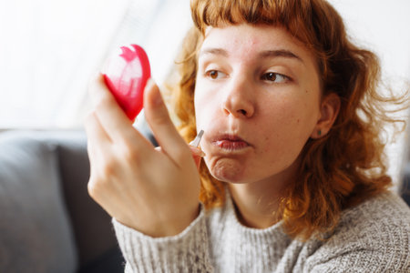 young woman looks at problematic facial skin in mirrorの写真素材