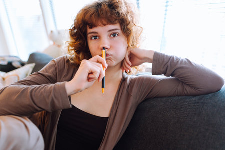 young woman at home writing notes in notebook while sitting on sofaの写真素材