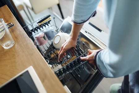 young woman putting dirty dishes into dishwasher at homeの写真素材